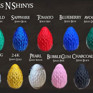 May include: A collection of 12 dragon eggs in various colors and finishes, including shiny red, green, blue, gold, copper, silver, white, black, pink, dark green, and yellow. The eggs are labeled with names like Ruby, Emerald, Sapphire, Tomato, Blueberry, Avocado, Lemon, Penny, Sterling, 24K, Pearl, Bubblegum, Charcoal, and Mallow.