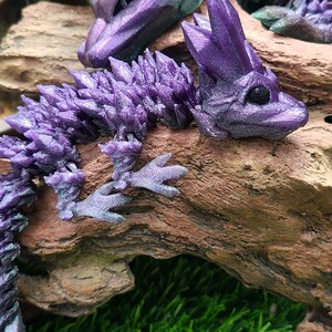 May include: A purple crystal dragon figurine with a spiky tail and a detailed face. The dragon is perched on a piece of driftwood.