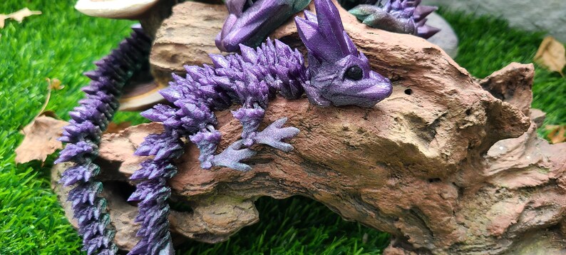 May include: A purple crystal dragon figurine with a spiky tail and a detailed face. The dragon is perched on a piece of driftwood.