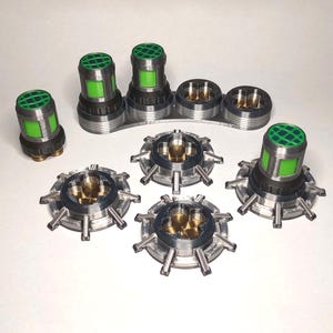 Pode incluir: Um conjunto de componentes metálicos e verdes, possivelmente para um dispositivo mecânico. As peças incluem elementos cilíndricos com tampas de malha verde e componentes circulares com extensões radiais. Dispostos sobre uma superfície branca.