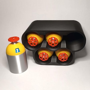 Può includere: Un contenitore nero stampato in 3D con quattro oggetti gialli e rossi a forma di valvola. È presente anche un cilindro giallo e argento separato con la parte superiore rossa e il numero 7. Gli oggetti sono probabilmente componenti di giocattoli o modelli.