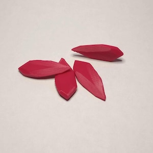 May include: Several bright red, petal-shaped objects are scattered on a white surface. The objects have a faceted design, with multiple flat surfaces creating a geometric appearance. The objects are likely decorative or craft elements.