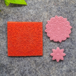 May include: Three rubber stamps with intricate mandala designs. The largest stamp is pink and features a circular design. The smaller stamps are red and pink and feature a square and a star design.