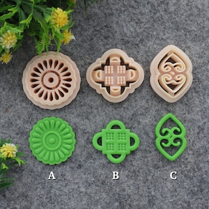 Puede incluir: Seis cortadores de galletas, tres son rosados y tres son verdes. Los cortadores rosados tienen forma de flor, cuadrado con un patrón de cuadrícula y espiral. Los cortadores verdes tienen forma de flor, cuadrado con un patrón de cuadrícula y espiral.