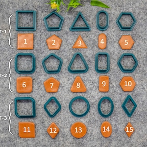 Pode incluir: Uma coleção de quinze cortadores de formas geométricas verde-azulado e laranja e suas formas correspondentes. As formas incluem quadrados, pentágonos, triângulos, ovais, hexágonos, círculos e diamantes. As formas estão dispostas em três conjuntos, rotulados SET-1, SET-2 e SET-3.