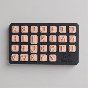 Puede incluir: Un juego de sellos rectangulares negros con el alfabeto en letras de color melocotón claro. Las letras están en una fuente de bloque. Las palabras "Goto Clay Tools" están impresas en la esquina inferior derecha.