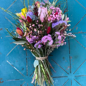 May include: A bouquet of pink, yellow, and purple flowers with green stems and leaves. The flowers are tied together with twine.