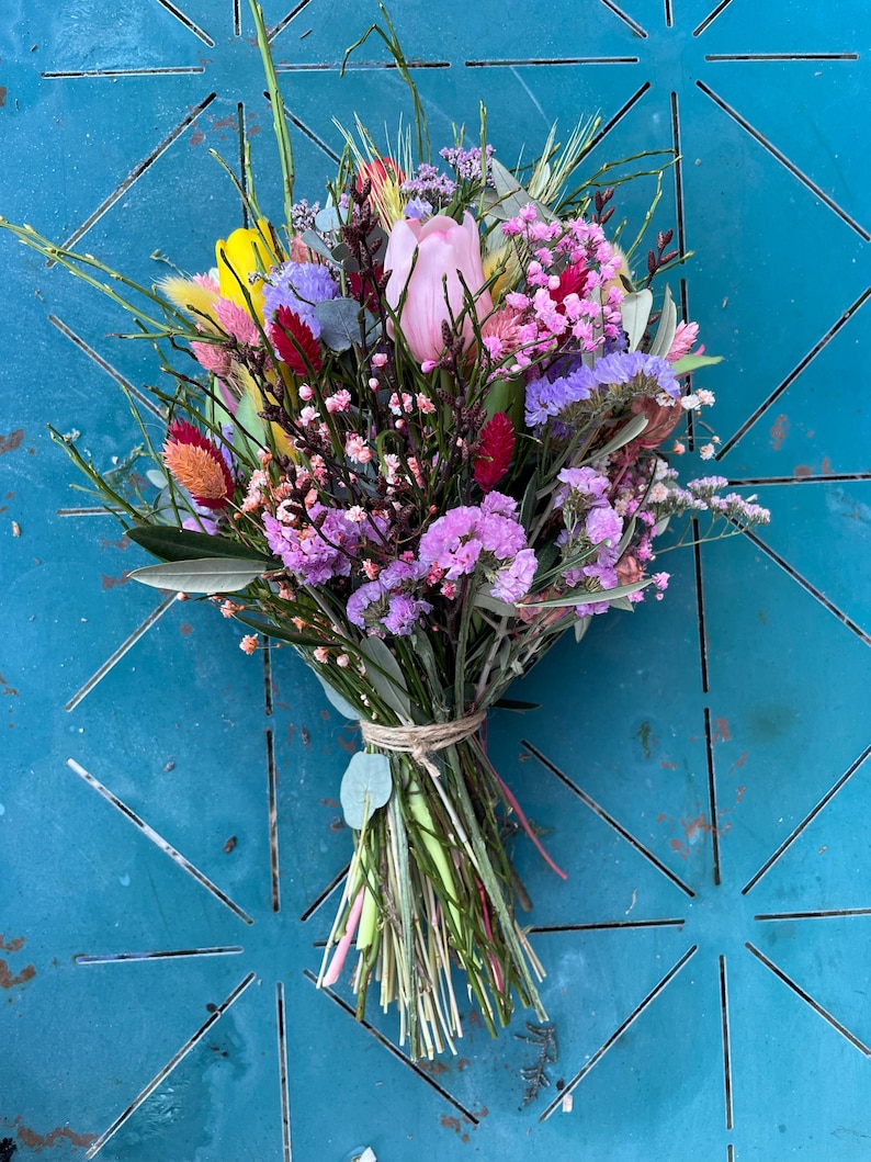 May include: A bouquet of pink, yellow, and purple flowers with green stems and leaves. The flowers are tied together with twine.
