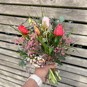 May include: A vibrant bouquet of fresh-cut flowers, featuring red and pink tulips, small white and pink blossoms, and green foliage. The bouquet is hand-tied with twine, creating a natural and rustic aesthetic.