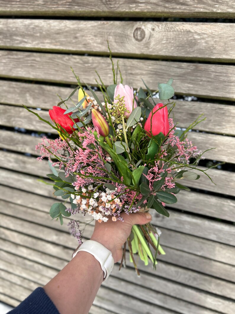 May include: A vibrant bouquet of fresh-cut flowers, featuring red and pink tulips, small white and pink blossoms, and green foliage. The bouquet is hand-tied with twine, creating a natural and rustic aesthetic.
