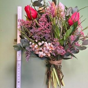 May include: A vibrant bouquet of flowers, featuring red tulips, pink and white filler flowers, and green foliage. The stems are tied with twine. The bouquet is approximately 12 inches long.