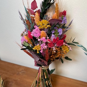 May include: A dried flower bouquet with a variety of colors, including pink, red, yellow, orange, and purple. The bouquet is tied with twine and includes dried grasses and other natural elements.