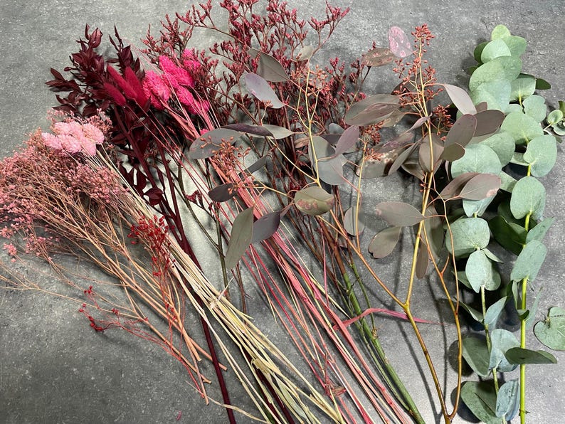 May include: A collection of dried flowers and foliage in shades of pink, red, and green. The arrangement includes eucalyptus, statice, and other textured stems, perfect for crafting or home decor.