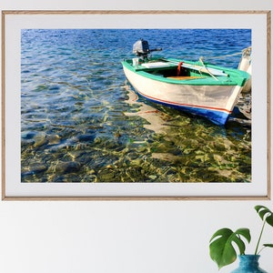 K&ouml;nnte beinhalten: Ein gerahmtes Foto eines kleinen, wei&szlig;en Bootes mit gr&uuml;nem Streifen und blauem Rand, das in klarem, flachem Wasser vor Anker liegt. Das Boot hat einen kleinen Au&szlig;enbordmotor am Heck.
