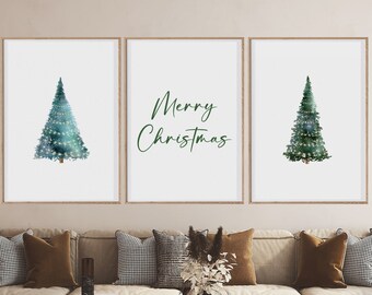 Pode incluir: Três impressões emolduradas com um design de estilo aquarela de árvores de Natal e o texto "Feliz Natal". As impressões estão penduradas em uma parede bege acima de um sofá bege com almofadas marrons.