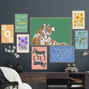 May include: A living room interior with a dark grey wall featuring a collection of framed prints. The prints include a tiger, a zebra, a floral design, a tree, and a quote that reads "Be happy, life is good". There is a dark wooden media console with a lamp and a white armchair.