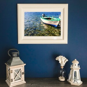 K&ouml;nnte beinhalten: Ein gerahmtes Foto eines kleinen gr&uuml;n-wei&szlig;en Bootes mit Motor in klarem blauen Wasser. Das Boot ist in seichtem Wasser mit felsigem Grund verankert.