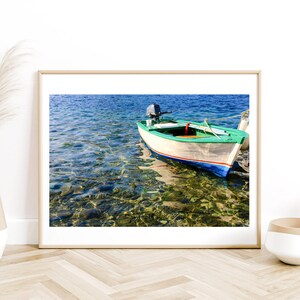 K&ouml;nnte beinhalten: Ein kleines, wei&szlig;es Holzboot mit einem gr&uuml;nen Streifen und blauen Verzierungen liegt in klarem, blauem Wasser vor Anker. Das Boot hat einen kleinen Au&szlig;enbordmotor und ist von Felsen und Seegras umgeben.