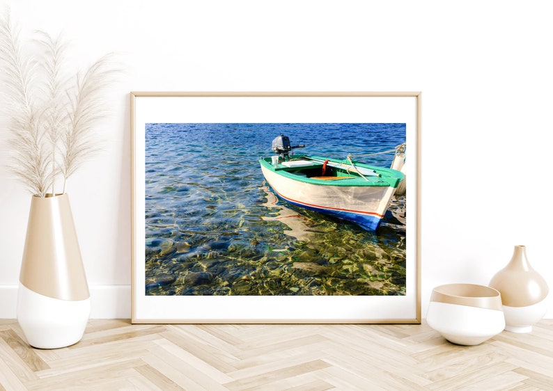 K&ouml;nnte beinhalten: Ein kleines, wei&szlig;es Holzboot mit einem gr&uuml;nen Streifen und blauen Verzierungen liegt in klarem, blauem Wasser vor Anker. Das Boot hat einen kleinen Au&szlig;enbordmotor und ist von Felsen und Seegras umgeben.