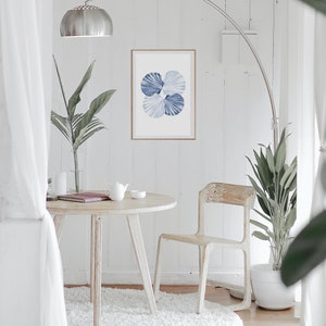 Puede incluir: Una mesa redonda blanca con una silla blanca y una alfombra blanca. Una impresi&oacute;n de acuarela azul y blanca de conchas marinas cuelga de la pared sobre la mesa. Una planta en maceta est&aacute; en la esquina de la habitaci&oacute;n.