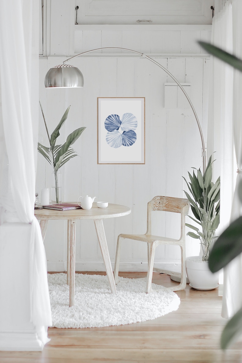 Puede incluir: Una mesa redonda blanca con una silla blanca y una alfombra blanca. Una impresi&oacute;n de acuarela azul y blanca de conchas marinas cuelga de la pared sobre la mesa. Una planta en maceta est&aacute; en la esquina de la habitaci&oacute;n.