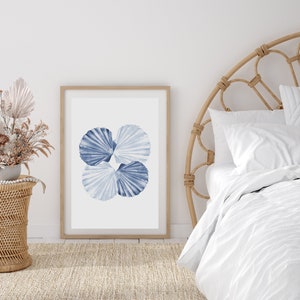 Puede incluir: Una impresi&oacute;n enmarcada de una pintura de acuarela de cuatro conchas azules sobre un fondo blanco. La impresi&oacute;n est&aacute; colgada en una pared blanca sobre una cabecera de mimbre.