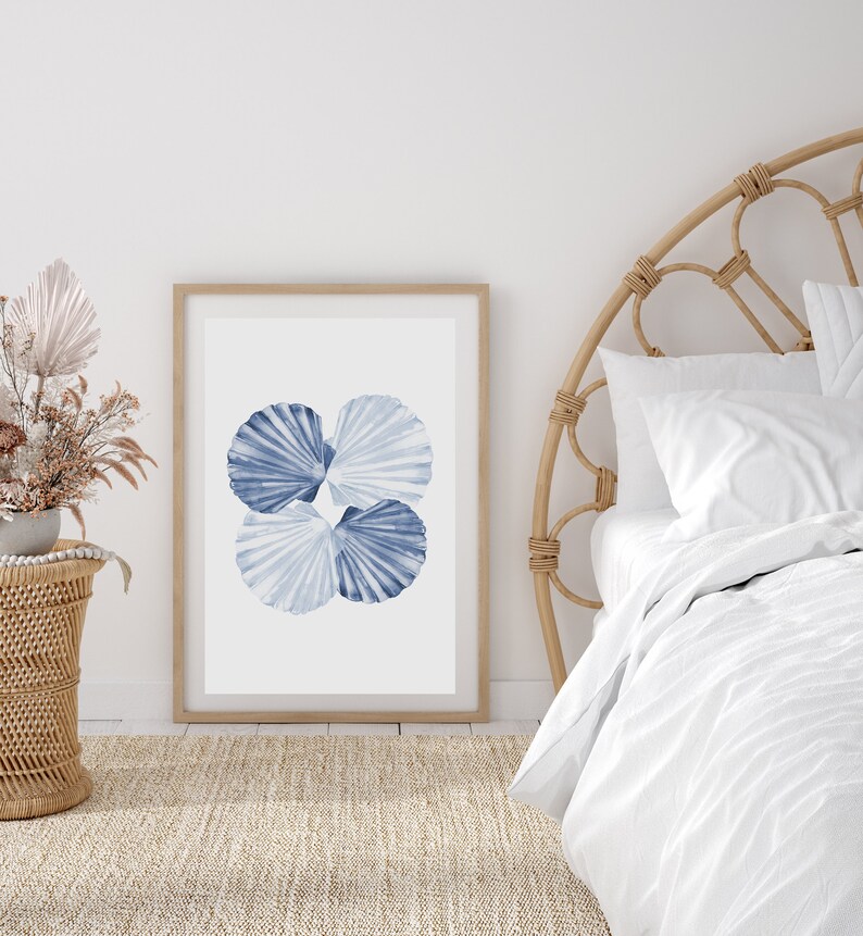 Puede incluir: Una impresi&oacute;n enmarcada de una pintura de acuarela de cuatro conchas azules sobre un fondo blanco. La impresi&oacute;n est&aacute; colgada en una pared blanca sobre una cabecera de mimbre.