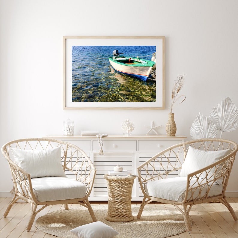 K&ouml;nnte beinhalten: Ein wei&szlig;es Holzboot mit gr&uuml;nem Streifen und blauer Verzierung liegt in klarem, blauem Wasser vor Anker. Das Boot hat einen kleinen Au&szlig;enbordmotor und ist von Felsen und Seegras umgeben.