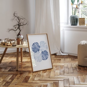 Puede incluir: Una impresi&oacute;n enmarcada de un dise&ntilde;o de conchas marinas azul y blanco sobre un fondo blanco. La impresi&oacute;n est&aacute; colgada en una pared blanca en una habitaci&oacute;n con suelo de madera.