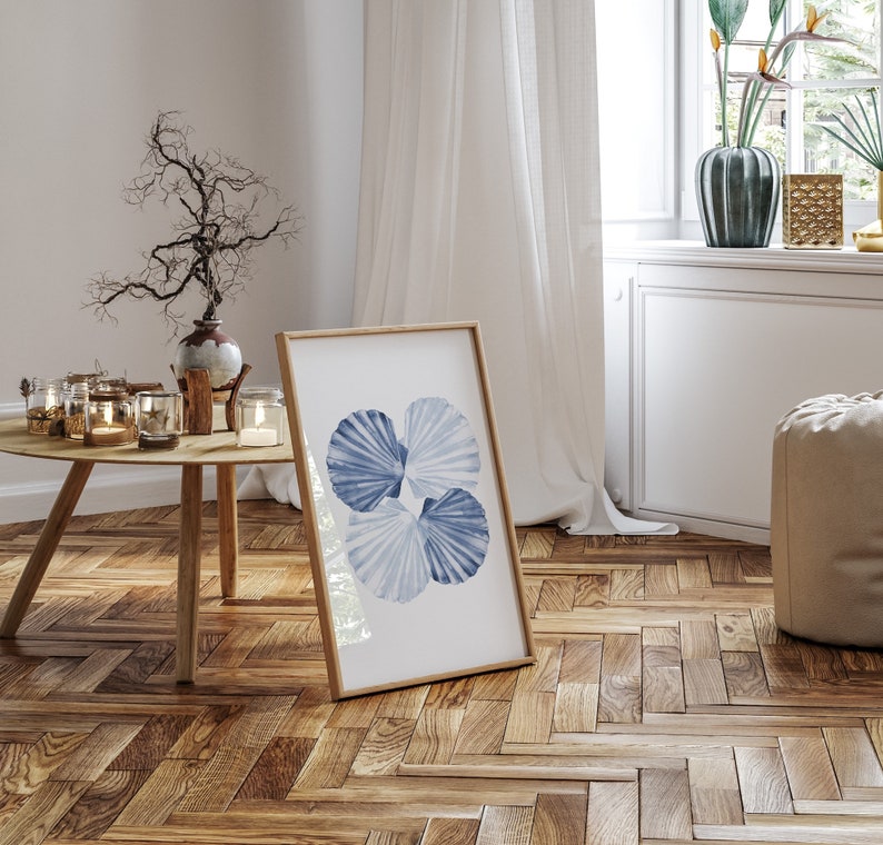 Puede incluir: Una impresi&oacute;n enmarcada de un dise&ntilde;o de conchas marinas azul y blanco sobre un fondo blanco. La impresi&oacute;n est&aacute; colgada en una pared blanca en una habitaci&oacute;n con suelo de madera.
