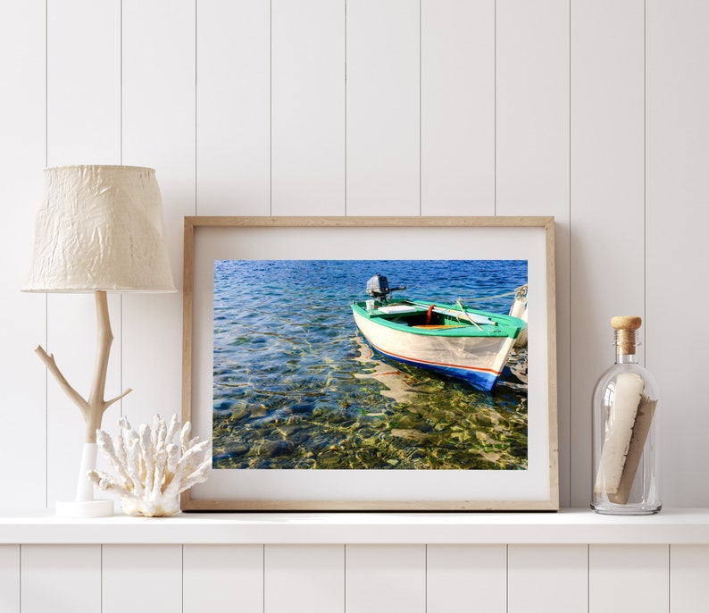 K&ouml;nnte beinhalten: Ein gerahmtes Foto eines kleinen, gr&uuml;n-wei&szlig;en Bootes mit einem Au&szlig;enbordmotor, das in klarem, blauem Wasser schwimmt. Das Wasser ist flach und der Grund ist sichtbar, mit Felsen und Seegras.