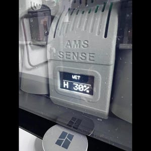 Puede incluir: Primer plano de un dispositivo gris con el texto "AMS SENSE" y una pantalla que muestra "WET" y "H 30%". El dispositivo es parte de un sistema m&aacute;s grande, con otros componentes visibles. El nivel de humedad es del 30%.
