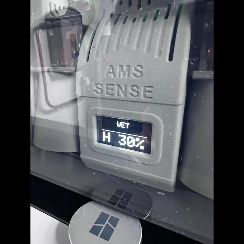 Puede incluir: Primer plano de un dispositivo gris con el texto "AMS SENSE" y una pantalla que muestra "WET" y "H 30%". El dispositivo es parte de un sistema m&aacute;s grande, con otros componentes visibles. El nivel de humedad es del 30%.
