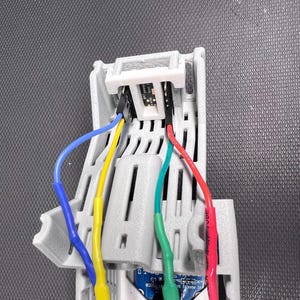 Puede incluir: Primer plano de un componente electr&oacute;nico de pl&aacute;stico gris con m&uacute;ltiples cables de colores conectados. Los cables son azules, amarillos, verdes y rojos. El componente tiene ranuras y aberturas.
