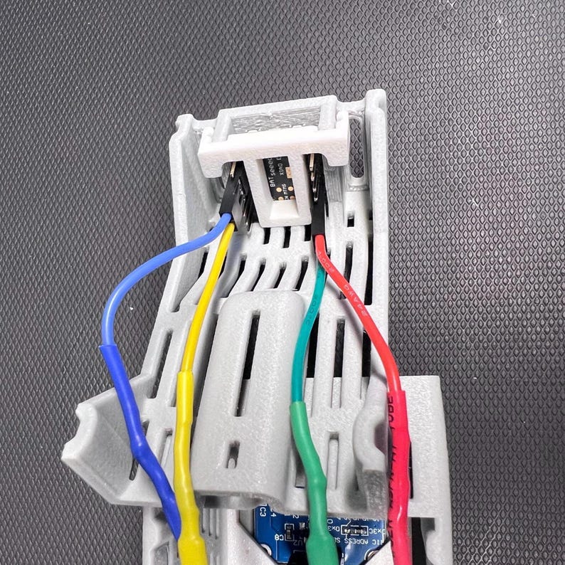 Puede incluir: Primer plano de un componente electr&oacute;nico de pl&aacute;stico gris con m&uacute;ltiples cables de colores conectados. Los cables son azules, amarillos, verdes y rojos. El componente tiene ranuras y aberturas.