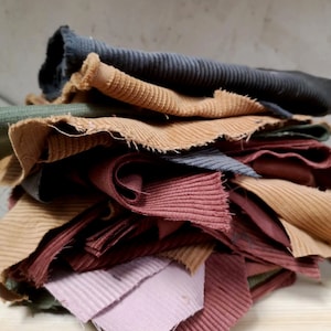 May include: A pile of fabric scraps in various shades of brown, pink, and blue. The fabric is a corduroy material with a ribbed texture.