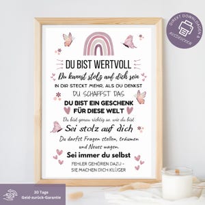 Könnte beinhalten: Gerahmter Druck mit hellem Holzrahmen, mit dem Text "DU BIST WERTVOLL" und weiteren deutschen Sätzen in dekorativer Schrift. Der Druck enthält Illustrationen von Schmetterlingen, Herzen und einem Regenbogen. Eine Kerze steht unten rechts.