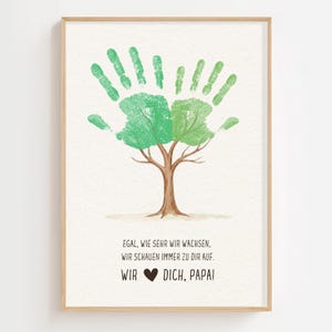 Peut inclure: Une affiche encadrée avec un motif d'arbre créé à partir d'empreintes de mains vertes. L'arbre a un tronc et des branches bruns, les empreintes de mains formant les feuilles. Le texte en bas se lit : "EGAL, WIE SEHR WIR WACHSEN, WIR SCHAUEN IMMER ZU DIR AUF. WIR ❤️ DICH, PAPA!"