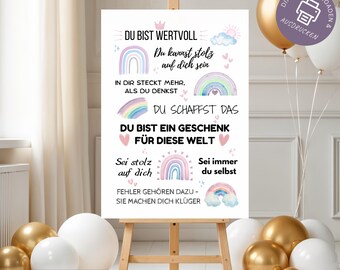 May include: A white poster on a wooden easel with German text and rainbow illustrations. The text includes phrases like "You are valuable" and "You can be proud of yourself." Gold and white balloons are in the background.