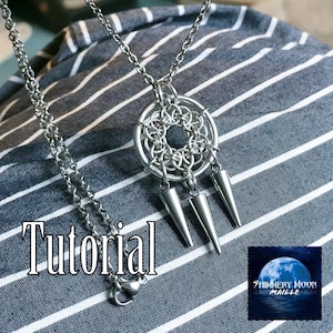 以下が含まれることがあります： チェーンメイルスタイルのペンダントが付いたシルバーカラーのネックレス。中央の円形デザインと3つの円錐形のダングルが特徴です。「Tutorial」という単語が画像に表示されています。ネックレスはストライプの背景に配置されています。