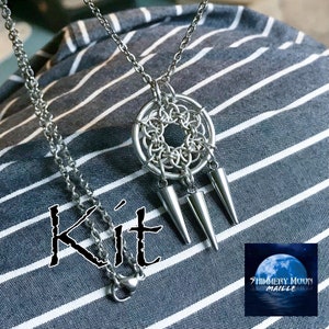 May include: A silver chain necklace with a silver pendant featuring a circular design with three spikes hanging from the bottom. The pendant is made of chainmaille and the text "Kit" is visible in the image. The text "Shimmery Moon Maille" is also visible in the image.