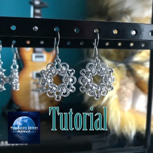 Puede incluir: Un par de pendientes de malla de plata en forma de copo de nieve, colgados de un expositor negro. Los pendientes se muestran sobre un fondo borroso de una guitarra y un objeto amarillo difuso. El texto "Tutorial" está escrito en letras grandes, negritas y verdes debajo de los pendientes.
