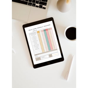 May include: A self-care weekly tracker on a tablet with a black frame. The tracker has a list of self-care goals, a calendar, and a mood tracker. The tablet is on a white surface with a laptop, a cup of coffee, a vase, and a pen.