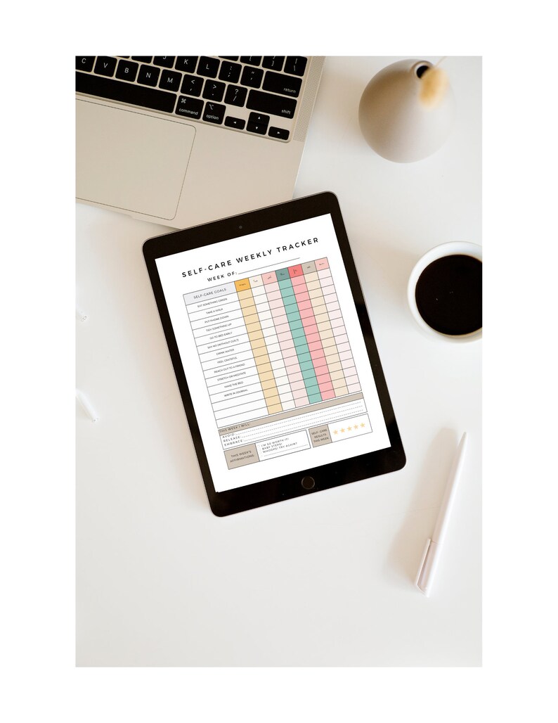 May include: A self-care weekly tracker on a tablet with a black frame. The tracker has a list of self-care goals, a calendar, and a mood tracker. The tablet is on a white surface with a laptop, a cup of coffee, a vase, and a pen.