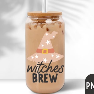 Puede incluir: Un vaso de vidrio transparente lleno de una bebida cremosa, con una tapa de bamb&uacute; y una pajita plateada. El vaso est&aacute; decorado con un dise&ntilde;o de sombrero de bruja beige con estrellas blancas y las palabras "witches BREW" en negro. Una bebida festiva para Halloween.