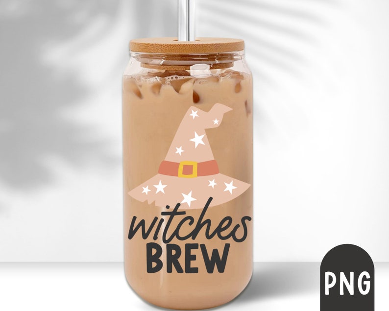 Puede incluir: Un vaso de vidrio transparente lleno de una bebida cremosa, con una tapa de bamb&uacute; y una pajita plateada. El vaso est&aacute; decorado con un dise&ntilde;o de sombrero de bruja beige con estrellas blancas y las palabras "witches BREW" en negro. Una bebida festiva para Halloween.