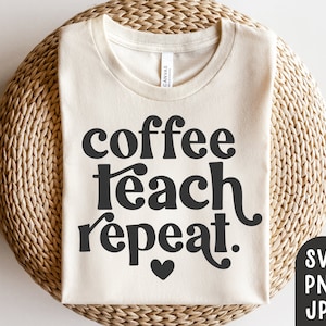 May include: Cream-colored t-shirt with the words "coffee teach repeat" in a bold, black font, with a small heart. The shirt is displayed on a woven, beige surface. The shirt is a crew neck style.