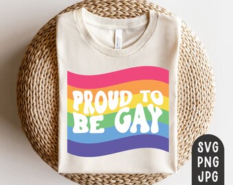 Puede incluir: Una camiseta color crema con el texto "PROUD TO BE GAY" en blanco, sobre un fondo de arcoíris. La camiseta se muestra sobre una superficie circular tejida. La imagen también incluye iconos de tipo de archivo: SVG, PNG y JPG.