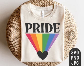Puede incluir: Camiseta color crema con la palabra "PRIDE" en letras negras sobre un diseño de arcoíris que irradia desde un corazón negro. La camiseta está hecha de un material suave y probablemente sea de corte unisex.