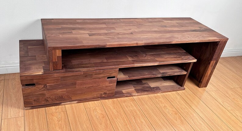 May include: A dark brown wooden entertainment center with a long top shelf, a pull-out drawer, and three open shelves.